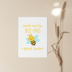 May include: A white card with the text "Thank you for BEE-ING a great teacher" in yellow. A cartoon bee with a smiling face is in the center of the card.