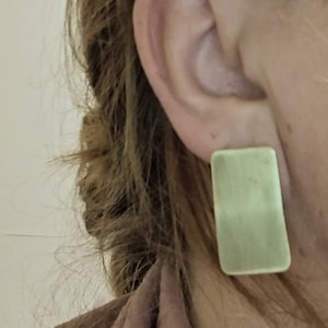 May include: A pair of light green rectangular earrings. The earrings are made of a smooth, polished material.