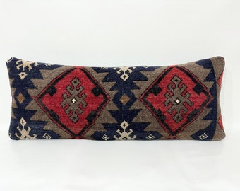 Puede incluir: Una almohada rectangular larga con un patrón geométrico en tonos de rojo, azul, marrón y blanco. La almohada está hecha de una tela tejida con una superficie texturizada.