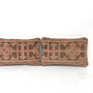 Puede incluir: Dos cojines rectangulares con un patr&oacute;n textil tejido en tonos rosa empolvado, marr&oacute;n y crema. La tela muestra un motivo geom&eacute;trico repetitivo con fibras texturizadas y gruesas, adem&aacute;s de bordes acabados, presentando un dise&ntilde;o uniforme.