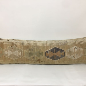 May include: A long, rectangular cushion with a beige background and a geometric pattern in shades of brown, grey, and white.