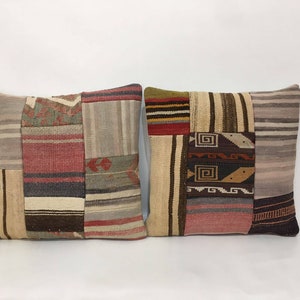 Può includere: Due cuscini quadrati con un design a patchwork. I cuscini sono realizzati con tessuti diversi in tonalità di marrone, beige, rosso e grigio. Il tessuto ha una trama tessuta.