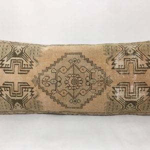 May include: A beige and brown patterned throw pillow with a geometric design. The pillow is made of a soft, woven fabric and has a fringed edge.