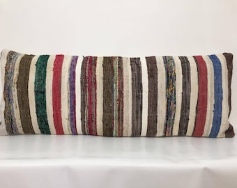May include: A long, rectangular pillow with a striped pattern in various colors, including brown, white, red, green, and blue. The pillow is made of woven fabric and has a rustic, handmade look.