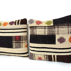 May include: Two decorative throw pillows with a patchwork design. The pillows are made of a beige fabric with black, brown, and white stripes. The pillows have colourful embroidered details.