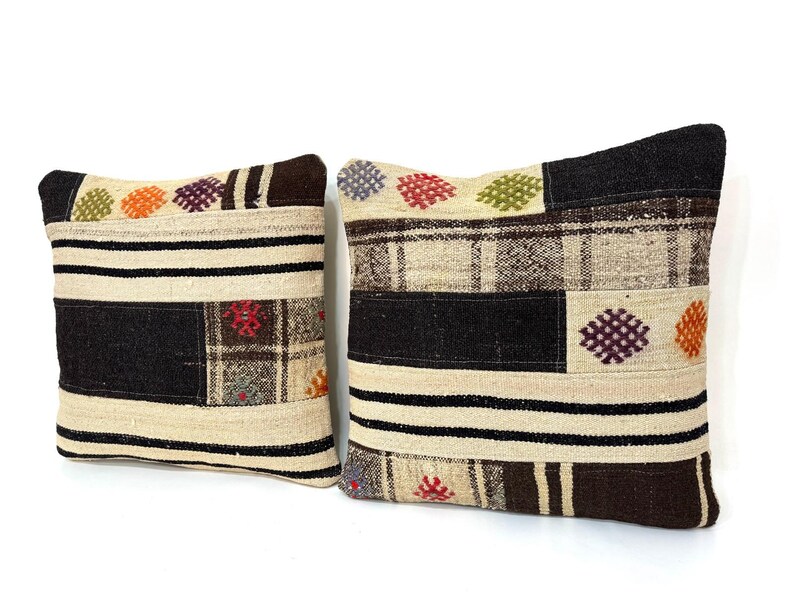 May include: Two decorative throw pillows with a patchwork design. The pillows are made of a beige fabric with black, brown, and white stripes. The pillows have colourful embroidered details.