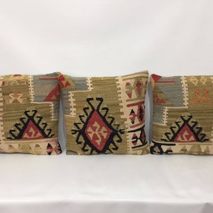 May include: Three decorative throw pillows with a geometric pattern in shades of beige, brown, red, and black. The pillows are made of woven fabric and have a traditional Turkish design.