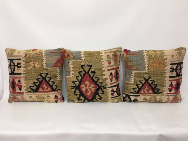 May include: Three decorative throw pillows with a geometric pattern in shades of beige, brown, red, and black. The pillows are made of woven fabric and have a traditional Turkish design.