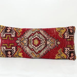 May include: A red, yellow, and white patterned throw pillow with a geometric design. The pillow is made of a soft, woven fabric.