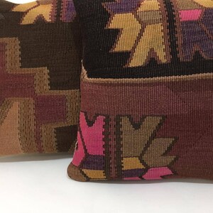 May include: Two decorative throw pillows with a woven pattern in shades of brown, pink, purple, and yellow. The pillows have a traditional, geometric design.