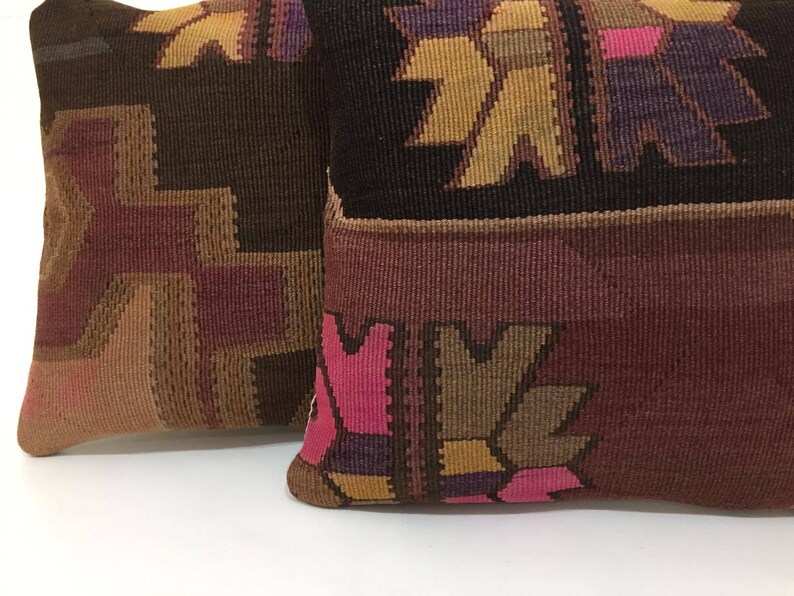 May include: Two decorative throw pillows with a woven pattern in shades of brown, pink, purple, and yellow. The pillows have a traditional, geometric design.