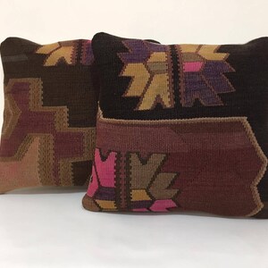 May include: Two decorative throw pillows with a geometric pattern in shades of brown, pink, and purple. The pillows are made of a woven fabric with a textured surface.