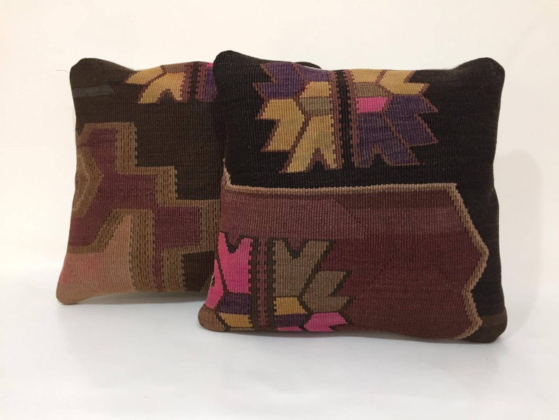 May include: Two decorative throw pillows with a geometric pattern in shades of brown, pink, and purple. The pillows are made of a woven fabric with a textured surface.