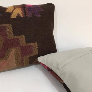 May include: Two decorative throw pillows, one with a brown background and a colorful geometric pattern, and the other with a plain light gray fabric.