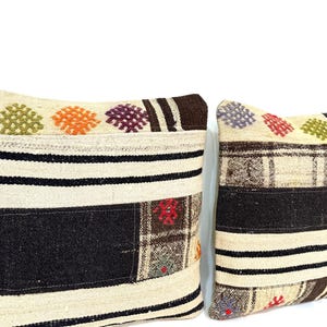 May include: Two decorative throw pillows with a patchwork design. The pillows are made of a beige fabric with brown, black, and colourful woven patterns.