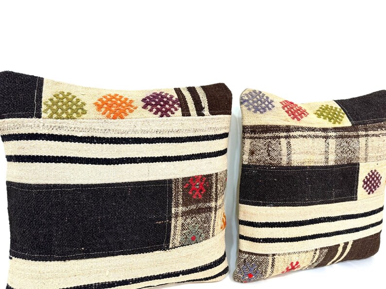 May include: Two decorative throw pillows with a patchwork design. The pillows are made of a beige fabric with brown, black, and colourful woven patterns.