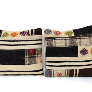 May include: Two decorative throw pillows with a patchwork design. The pillows are made of a beige fabric with black, brown, and colourful accents. The pillows have a woven texture and feature geometric patterns.