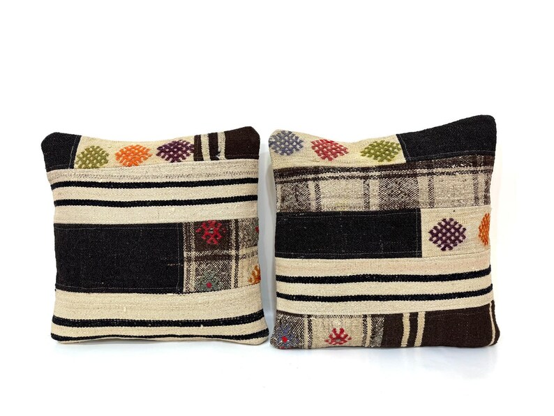 May include: Two decorative throw pillows with a patchwork design. The pillows are made of a beige fabric with black, brown, and colourful accents. The pillows have a woven texture and feature geometric patterns.