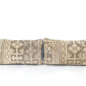 Könnte beinhalten: Zwei rechteckige Kissen mit einem beige-braunen geometrischen Muster. Die Kissen haben eine gewebte Textur und eine neutrale Farbpalette, passend für verschiedene Einrichtungsstile.