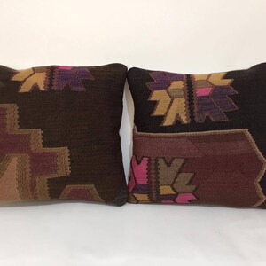 May include: Two square throw pillows with a brown, burgundy, pink, and gold geometric pattern. The pillows are made of a woven fabric.