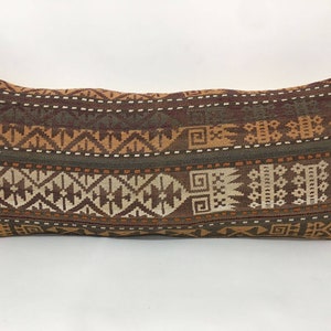 May include: A long, rectangular pillow with a brown, orange, and white geometric pattern. The pillow is made of a woven fabric and has a subtle texture.
