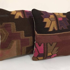 May include: Two decorative throw pillows with a woven pattern in shades of brown, pink, and purple. The pillows have a geometric design with a traditional look.