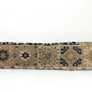 May include: A long, rectangular pillow with a traditional Persian-style design. The pillow is made of a woven fabric with a beige background and intricate patterns in shades of blue, green, and pink.