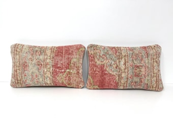 Puede incluir: Dos cojines rectangulares con un patrón desgastado y descolorido en tonos rojo apagado, verde salvia y beige. La tela muestra una apariencia texturizada y envejecida con intrincados motivos ornamentales repetitivos en la superficie.