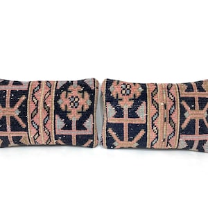 May include: Two rectangular decorative pillows with a geometric pattern. The pillows feature a navy blue background with pink, tan, and gray accents. The design includes stylized floral and geometric shapes. The pillows are placed side by side.