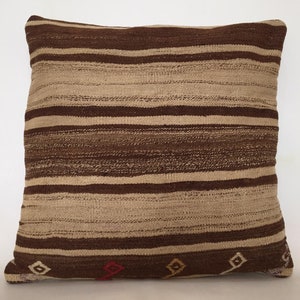 Puede incluir: Una almohada de tiro de rayas marrones y beige con un patrón tejido. La almohada tiene un sutil patrón de diamantes en la parte inferior.