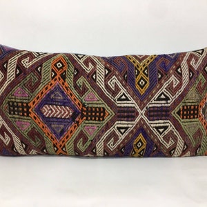May include: A long rectangular pillow with a colorful geometric pattern in shades of purple, orange, green, brown, and white. The pattern is intricate and features a variety of shapes, including diamonds, squares, and triangles.