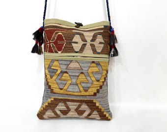 Può includere: Borsa a tracolla rettangolare con un motivo geometrico intrecciato nei toni del marrone, oro e grigio. La borsa ha una chiusura con cerniera e una tracolla intrecciata blu scuro. Nappe rosse, nere e bianche adornano i lati.