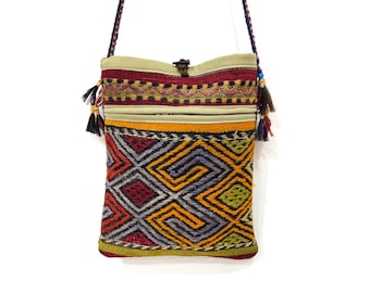 Può includere: Una colorata borsa a tracolla tessuta con un motivo geometrico in rosso, arancione, giallo e grigio. La borsa ha una parte superiore beige con cerniera e una tracolla intrecciata con nappe. La borsa misura circa 20 cm di larghezza e 25 cm di altezza.