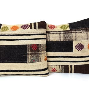 May include: Two decorative throw pillows with a patchwork design. The pillows are made of a beige fabric with black, brown, and red accents. The pillows feature a variety of geometric patterns and embroidered details.