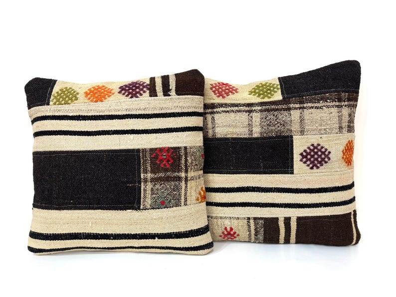 May include: Two decorative throw pillows with a patchwork design. The pillows are made of a beige fabric with black, brown, and red accents. The pillows feature a variety of geometric patterns and embroidered details.