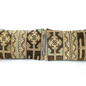 May include: Two rectangular throw pillows with a brown, beige, and teal geometric pattern. The pillows have a textured appearance and are placed side by side on a white background. The design features floral and linear elements.