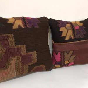 May include: Two decorative throw pillows with a geometric pattern in shades of brown, pink, and purple. The pillows are made of woven fabric and have a traditional design.