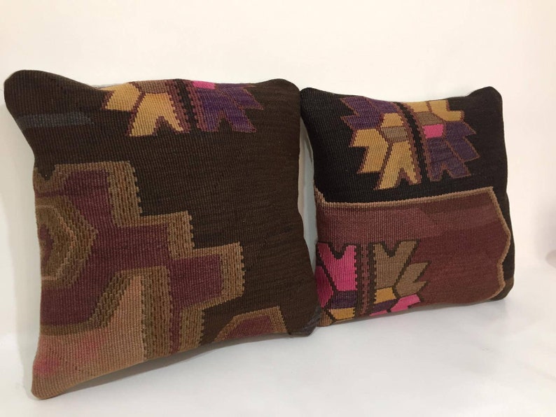 May include: Two decorative throw pillows with a geometric pattern in shades of brown, pink, and purple. The pillows are made of woven fabric and have a traditional design.