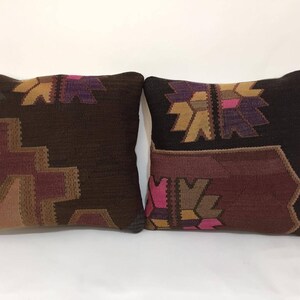 May include: Two decorative throw pillows with a traditional Turkish kilim pattern. The pillows are brown with pink, purple, and gold accents.