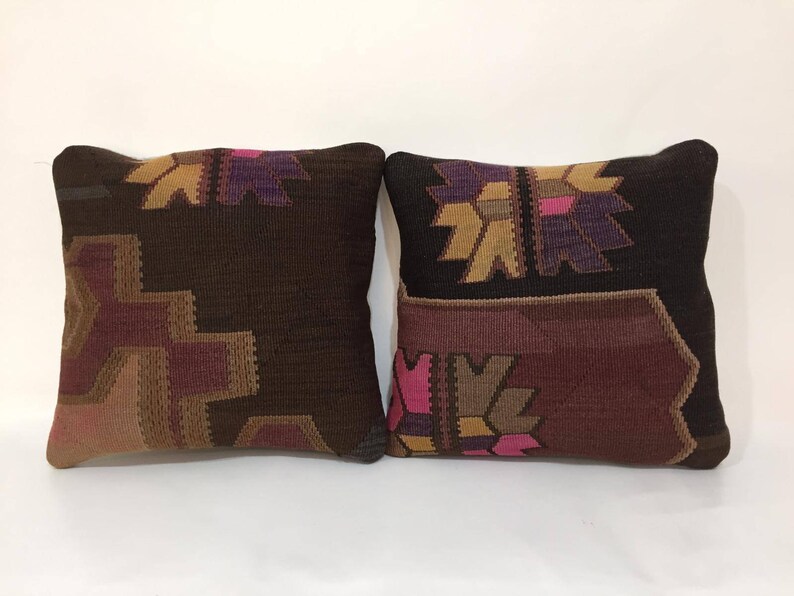 May include: Two decorative throw pillows with a traditional Turkish kilim pattern. The pillows are brown with pink, purple, and gold accents.