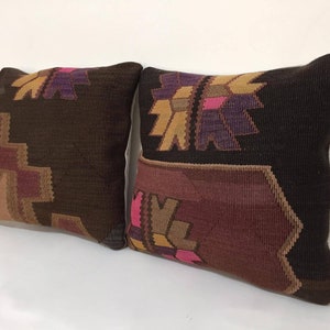 May include: Two decorative throw pillows with a brown, pink, and purple geometric pattern. The pillows are made of a woven fabric and have a soft, textured feel.
