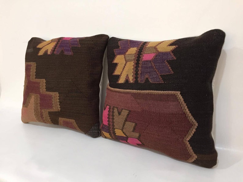 May include: Two decorative throw pillows with a brown, pink, and purple geometric pattern. The pillows are made of a woven fabric and have a soft, textured feel.