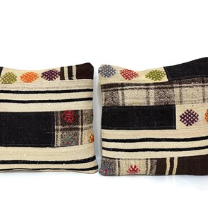 May include: Two square throw pillows with a patchwork design. The pillows are made of a beige fabric with black, brown, and white stripes. The pillows have colourful embroidered details.