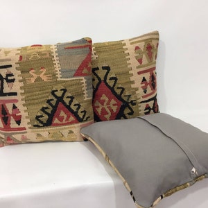 May include: Two decorative throw pillows with a geometric pattern in shades of beige, brown, red, and black. The pillows are made of woven fabric and have a zipper closure.