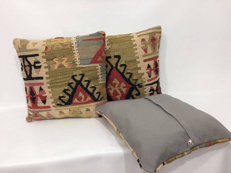 May include: Two decorative throw pillows with a geometric pattern in shades of beige, brown, red, and black. The pillows are made of woven fabric and have a zipper closure.