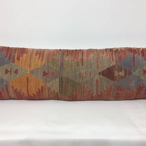 May include: A long, rectangular pillow with a geometric pattern in shades of red, orange, brown, and gray. The pillow is made of woven fabric and has a traditional, ethnic design.