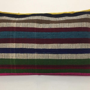 May include: A striped cushion with a variety of colours, including pink, green, blue, red, and brown. The cushion is made of a woven fabric and has a rectangular shape.