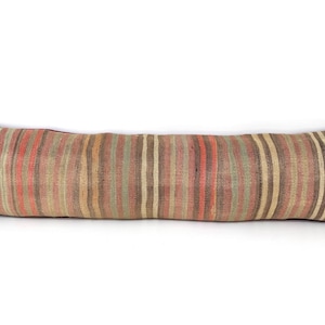 May include: A long, rectangular bolster pillow featuring a woven fabric cover with vertical stripes in muted shades of sage green, terracotta orange, dark brown, and cream. The textile has a textured appearance with visible weave patterns.