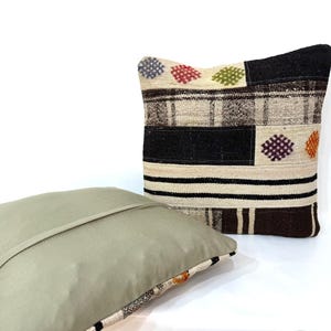 May include: Two decorative throw pillows, one with a beige background and a geometric pattern in black, brown, and white, and the other with a solid beige colour.
