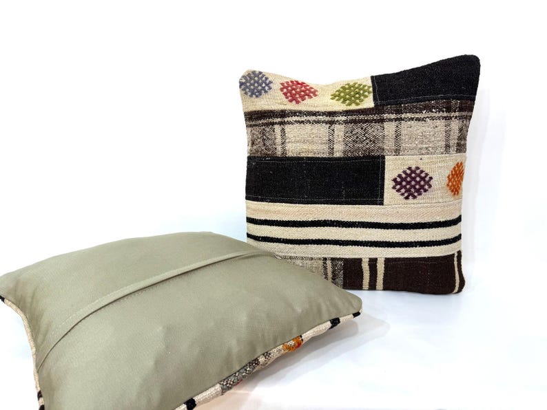 May include: Two decorative throw pillows, one with a beige background and a geometric pattern in black, brown, and white, and the other with a solid beige colour.